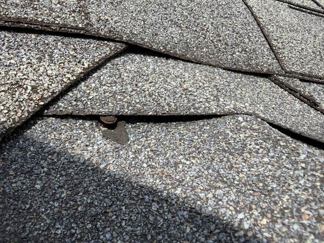 Rusted roofing nail backed out under a lifted shingle tab