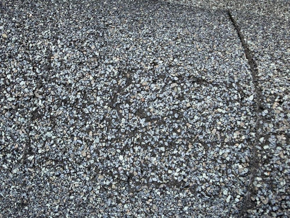 Close-up of a worn asphalt shingle with thin granule cover and dark asphalt showing between the granules