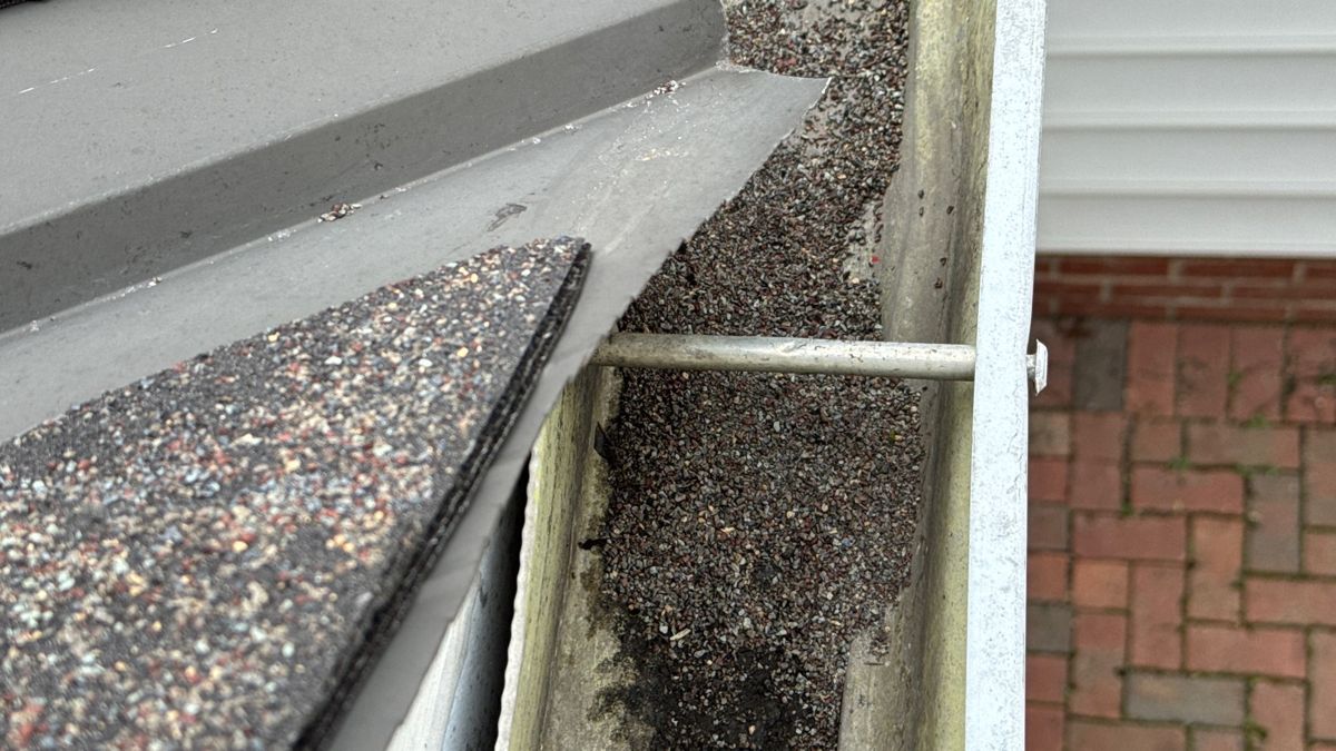 Layer of shingle granules and grit settled in the bottom of a gutter