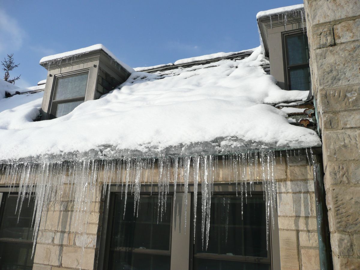 Ice dam and long icicles hanging from the edge of a snow-covered roof