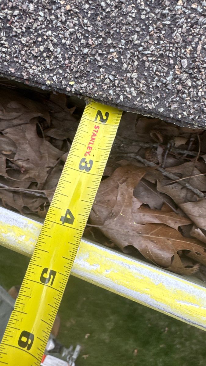 Tape measure standing in a gutter packed with about four inches of wet leaves