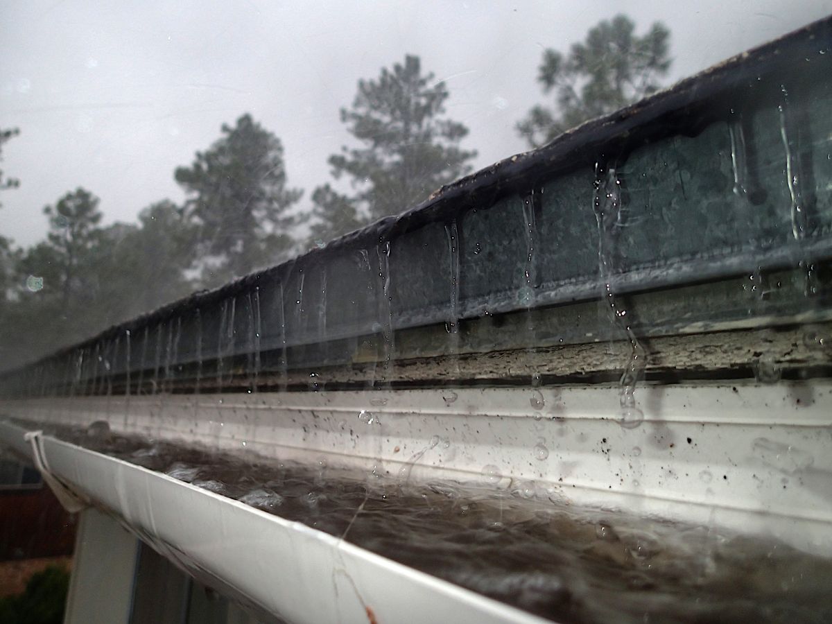 Rain pouring over the front edge of a gutter that needs cleaning