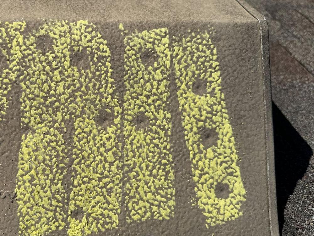 Metal roof vent rubbed with yellow chalk, with round hail dents showing as bare dimples