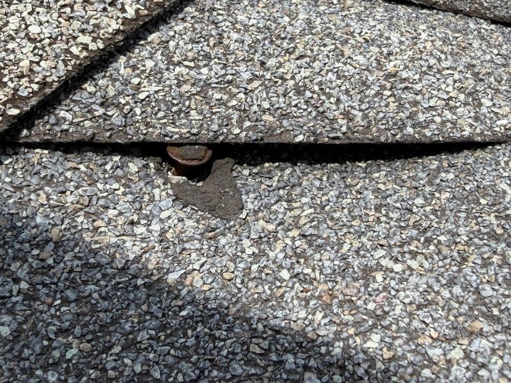 Backed-out roofing nail standing up under the lifted edge of the shingle above it