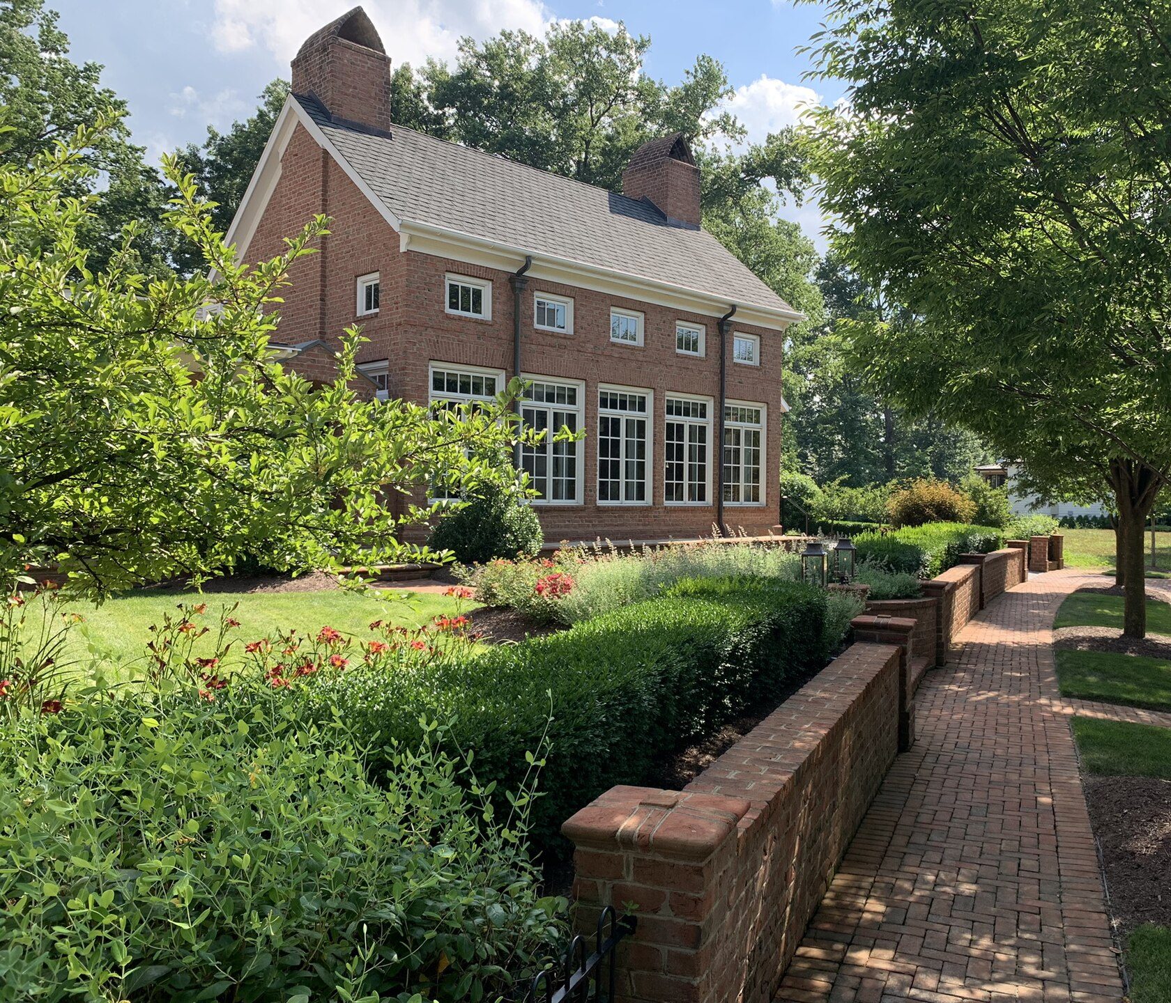 A Georgian red-brick home in New Albany with a gray shingle roof, two chimneys and a brick garden wall along the sidewalk