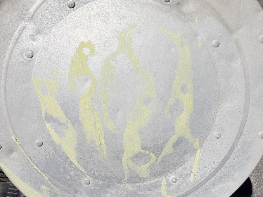Aluminum attic fan dome rubbed with yellow chalk showing round hail dents
