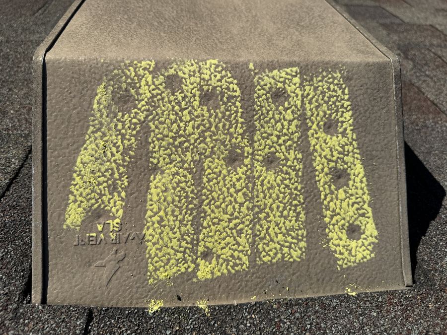 Metal box roof vent rubbed with yellow chalk so round hail dents show as bare spots