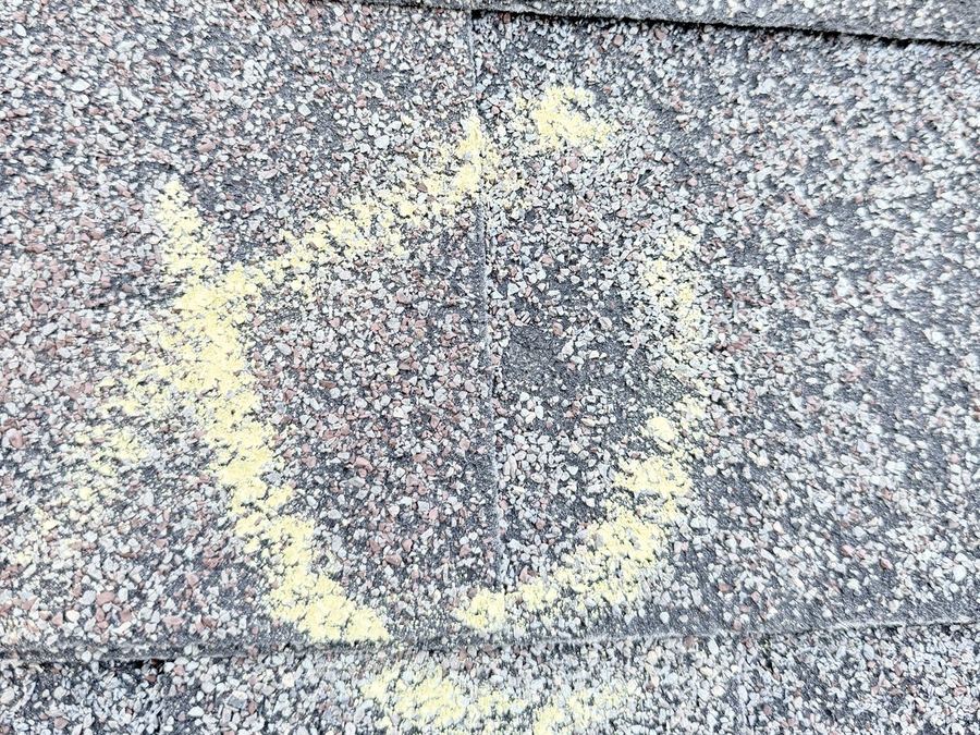 Hail hit on an asphalt shingle circled in yellow chalk during a roof inspection